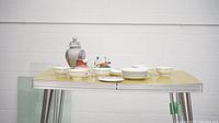 Front view of assorted ceramic items including ginger jar, plates, bowls, cups, and ceramic figurine on yellow tabletop