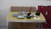Photo showing entire lot on yellow checkered table including plates, vases, swan figurine, and fruit dish.