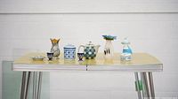 Eight assorted ceramic decorative items displayed on a yellow table including bud vases, jars, a figurine, and candle holders
