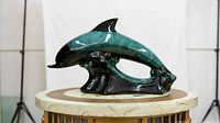 Full view of blue-green glazed ceramic dolphin sculpture on round table with marble top.