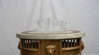 Crystal cream and sugar set displayed on antique table with carved lion head detail.