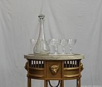 Photo showing the clear glass decanter with stopper and five matching glasses placed on a marble topped small table with decorative brown base.
