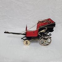 Side view of miniature horse carriage showing black and red paint with gold chains and wheels, detailing the craftsmanship.