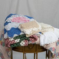Crocheted blankets and doilies stacked on a small wooden table with a light background