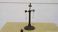 Photo showing the detailed view of the vintage metal lamp base with two pull chain sockets, cord, and decorative round base.