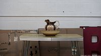 Light brown jug and basin sitting on a yellow retro table against cardboard boxes background.
