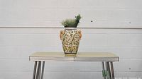 Front view of the decorative vase with artificial greenery on table against white wall.