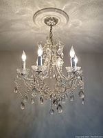 Chandelier hanging from ceiling with lights on, showing glass beads and teardrop pendants