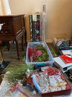 Christmas decorations and wrap including bins with fake greens, red berries, lighted tree branches, and stacks of wrapping paper.