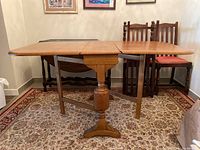 Full view of the wooden drop leaf table open, showing lengthened leaves and pedestal base with turned legs.
