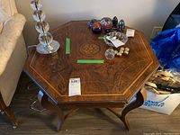 Octagonal wooden end table with decorative marquetry inlay on top, scratches and scuffs visible on surface, curved legs.