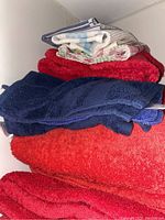 Photo showing stacked terry cloth towels in navy blue, dark red, and bright red colors with lighter fabric pieces on top