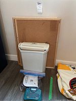 Paper shredder in front of three cork boards, two label makers partially visible. Shredder is white, cork boards have wooden frames.