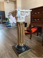 Full view of the column style pedestal plant stand showing body and decorative top, situated on floor near furniture.