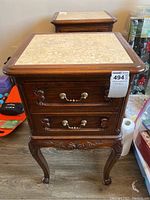 Front view of wooden side table showing marble top, two drawers with brass handles, and carved legs.