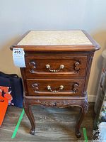Front and side view of the wood side table showing marble top, engraving detail, curved legs, brass handles on two drawers, and surface wear.