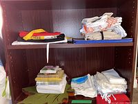 Photo showing shelf of assorted folded aprons, cloth napkins, and paper napkins in stacks and bundles.