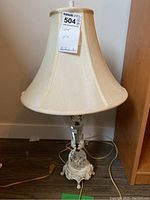Front view of vintage table lamp showing faceted crystal column, enameled metal base, and cream fabric shade.