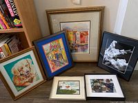 Set of five framed watercolour paintings and one framed black and white photograph displayed on floor, showing all artworks