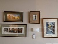 Photo showing all four framed artworks hanging on a wall: three watercolours and one larger print with an architectural scene.