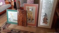Overview of four pieces arranged side by side: green-matted parrot print, carved wood relief panel, dog portrait, map/wildlife print