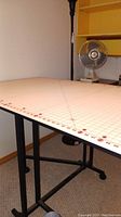 Top view of the fabric cutting board on the folding table, showing grid lines and measurement markings.