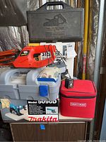 Overall lot showing Craftsman belt sander case, Black & Decker cordless trimmer, Dremel toolkit case, Makita handsaw box, Craftsman level soft case.