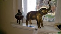 Brass elephant figurine and bronze tripod incense burner on windowsill