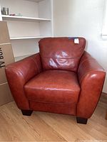 Front view of one reddish-brown leather club chair with loose back cushion and squared arms