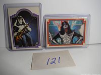 Front view of two Ace Frehley trading cards in protective holders, showing card numbers and artwork.
