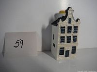 Front and one side view of the ceramic miniature Delft-style house liquor bottle with blue and black detailing and yellow stopper.