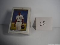 Front view of Frank Thomas Rookie Card in protective sleeve next to lot number 65.