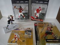 Four sports action figures displayed in original blister packaging including two NFL Series 22 figures and two other sports figures.