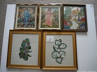 Five framed vintage needlepoint artworks laid out on a white surface showing various scenes and floral designs.
