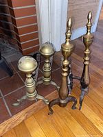 Both sets of brass andirons placed by fireplace showing front and side view.