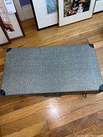 Closed gray fabric-covered carry case with black corner protectors on a wooden floor.