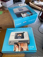 Two Canon Selphy compact photo printers in original boxes, models CP510 and CP730.