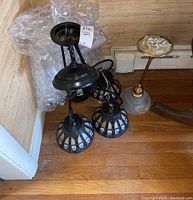 Overview of the two ceiling light fixtures on hardwood floor next to bubble wrap and two electrical boxes.