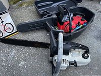 Two gas chainsaws in black plastic cases; one red Craftsman, another white/black unknown brand.