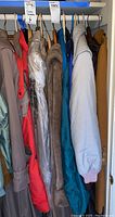 Closet view of seven coats and jackets hanging side by side in assorted colors including red, beige, brown, blue, and tan.