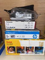 Shows Kodak DC3800, Panasonic Lumix S3, and HP Photosmart M547 cameras with their respective boxes and some accessories wrapped in plastic.
