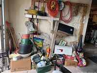 Overview of garden supplies including watering cans, pots, sprayers, extension cords, and lawn products in garage corner