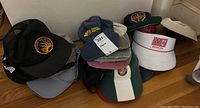 Overview photo of the various hats stacked on the floor showing multiple logos and colors.