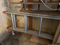 Full view of the metal extension ladder lying on the floor against a wall, showing the length and construction of the ladder.