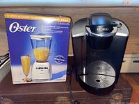 Oster 12-speed Osterizer blender model 6641 in sealed box and Keurig coffee maker side by side on shelf.