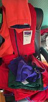 Photo showing Patagonia sweatshirt with tag indicating size L and coral color. Sweatpants underneath in blue and green. Various folded clothing items visible.