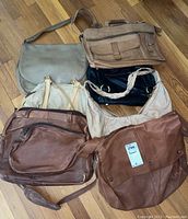 Top view of seven large leather-like and suede-like over the shoulder purses in different colors and styles