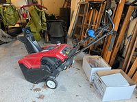 Red and black Toro Power Clean 4-cycle snow blower shown in garage setting with boxes and other items in background.