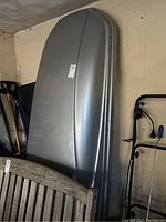 Full view of silver Thule roof cargo box leaning against wall, shows overall shape and scratches
