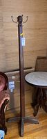 Full view of vintage wooden tall coat rack standing upright showing wooden shaft, base, and four metal hooks at top.